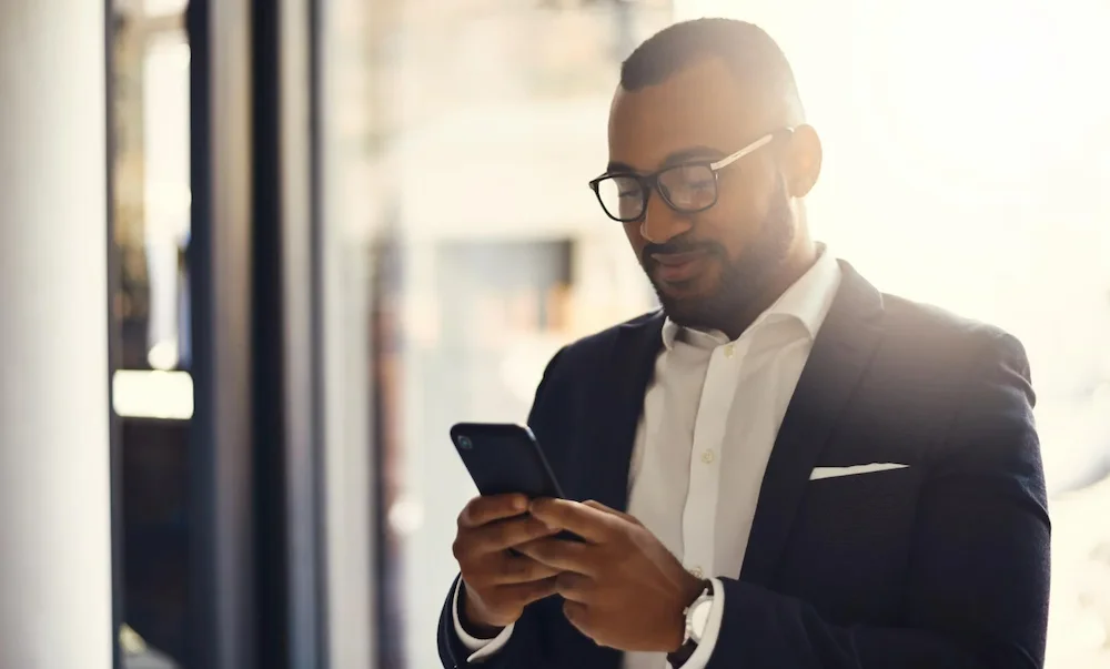 Homem negro de terno, dono de uma rede de supermercados, usando celular para conferir a gestão dos resultados no monitor da Solidcon.