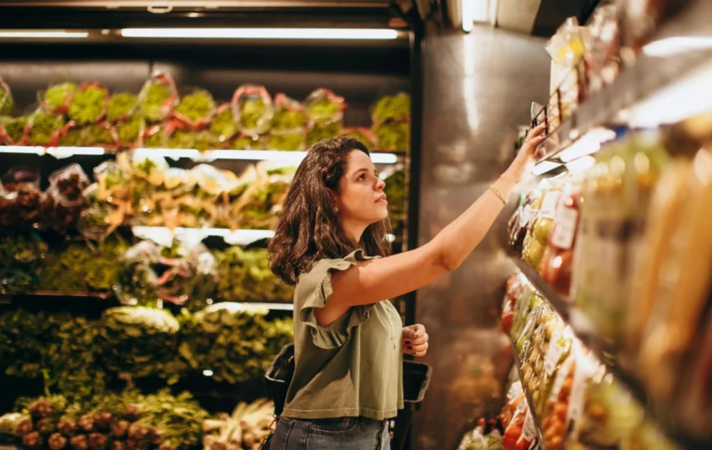 Mulher escolhendo produtos em prateleiras organizadas de supermercado, ilustrando a importância da padronização de cadastro para a organização física da loja.
