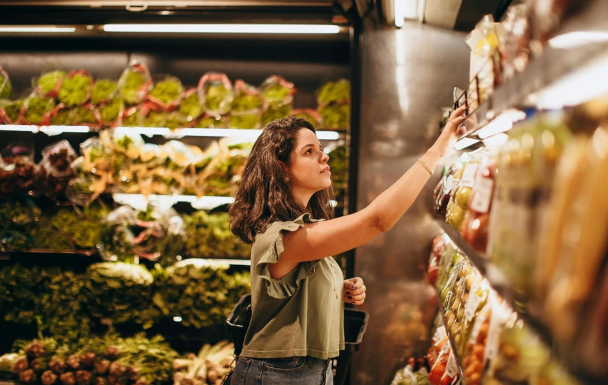 Mulher escolhendo produtos em prateleiras organizadas de supermercado, ilustrando a importância da padronização de cadastro para a organização física da loja.